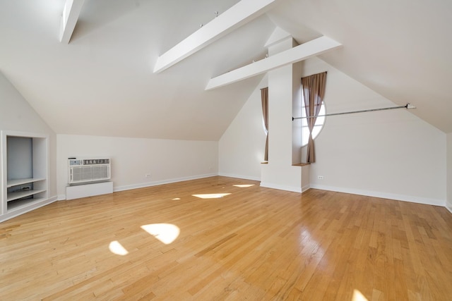 additional living space featuring light wood-type flooring, built in shelves, lofted ceiling, a wall unit AC, and baseboards