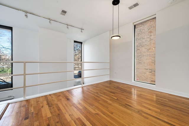 unfurnished room with hardwood / wood-style floors, a wall of windows, a healthy amount of sunlight, and visible vents