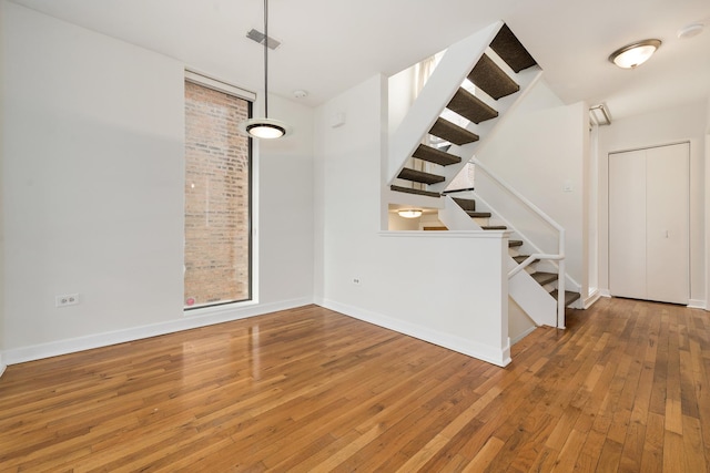 unfurnished dining area with hardwood / wood-style floors, stairs, and baseboards