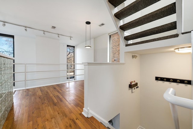 hall featuring a wealth of natural light, visible vents, rail lighting, and hardwood / wood-style flooring