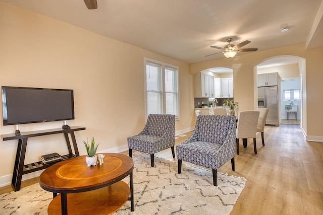 living area with arched walkways, baseboards, light wood-type flooring, and ceiling fan