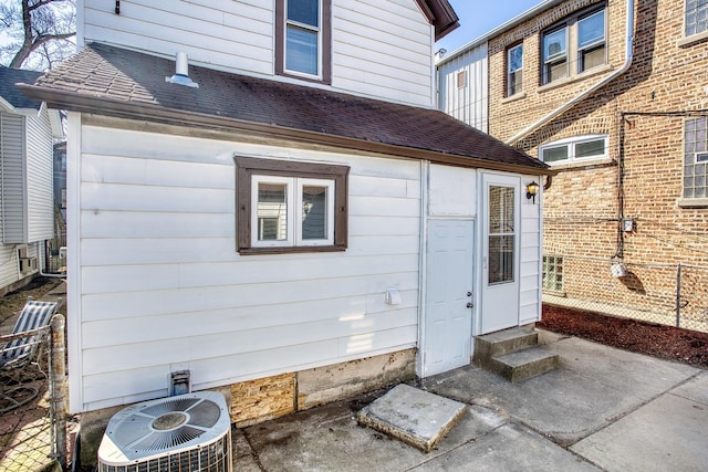 property entrance with a shingled roof, central AC, and fence