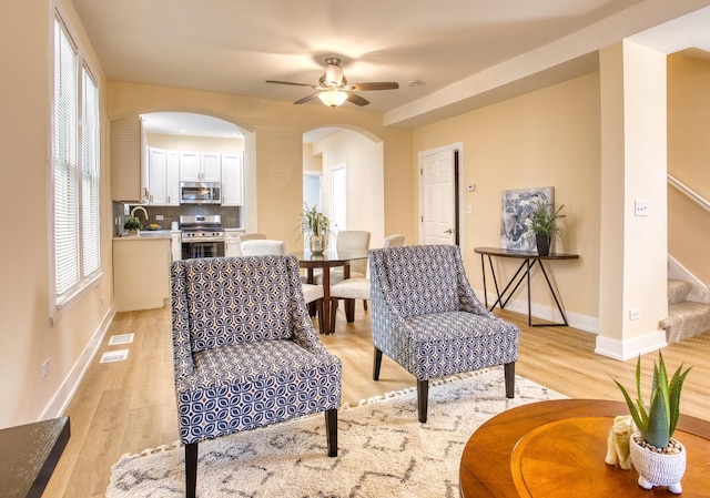 living area with stairway, baseboards, light wood-style flooring, arched walkways, and ceiling fan