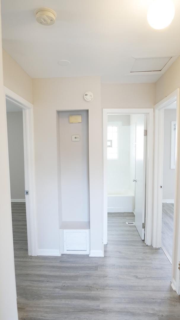 hall with attic access, wood finished floors, and baseboards