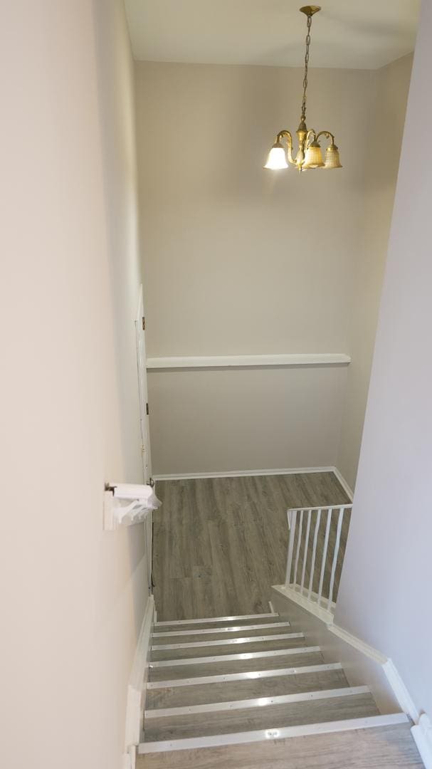 staircase with baseboards, a notable chandelier, and wood finished floors