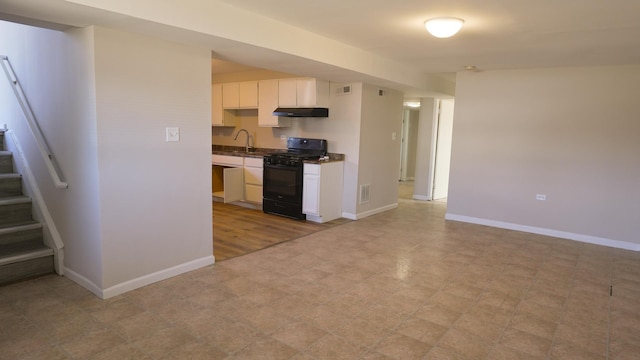 kitchen featuring black range with gas cooktop, baseboards, under cabinet range hood, and a sink