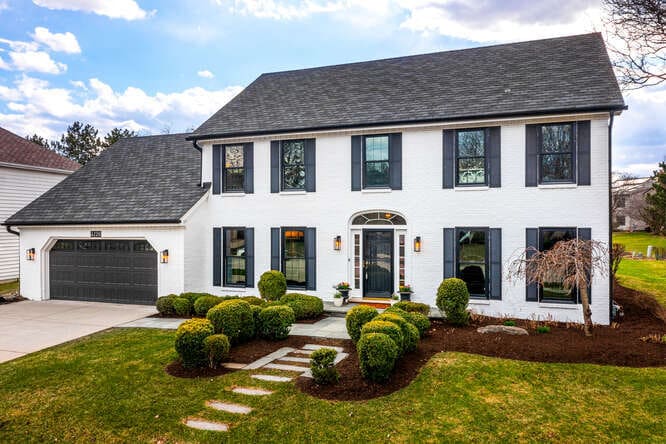 colonial house featuring stucco siding, roof with shingles, an attached garage, driveway, and a front lawn