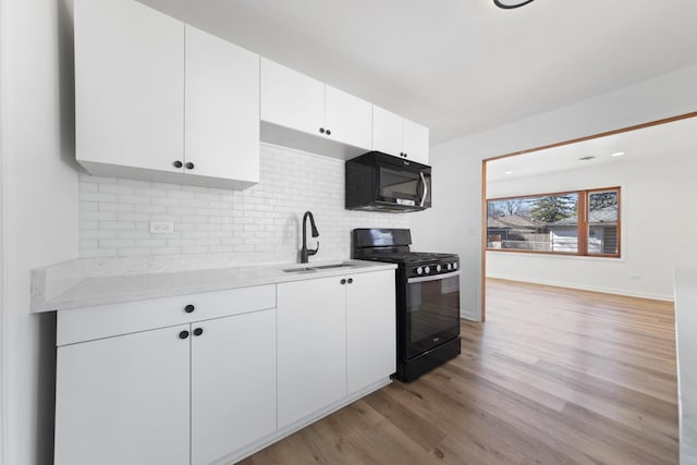 kitchen featuring tasteful backsplash, light wood-style flooring, white cabinets, a sink, and black appliances