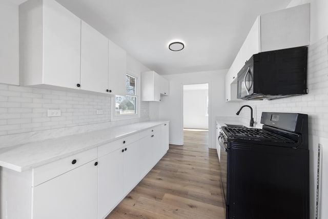 kitchen with white cabinets, light wood-style floors, backsplash, black appliances, and a sink