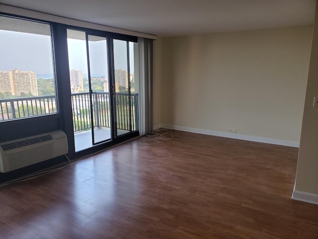 empty room featuring a wall of windows, wood finished floors, baseboards, a wall mounted air conditioner, and a city view