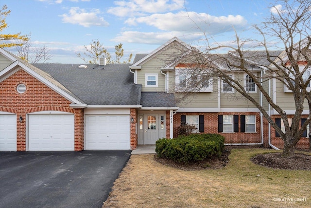 view of property featuring a front yard, driveway, a shingled roof, a garage, and brick siding