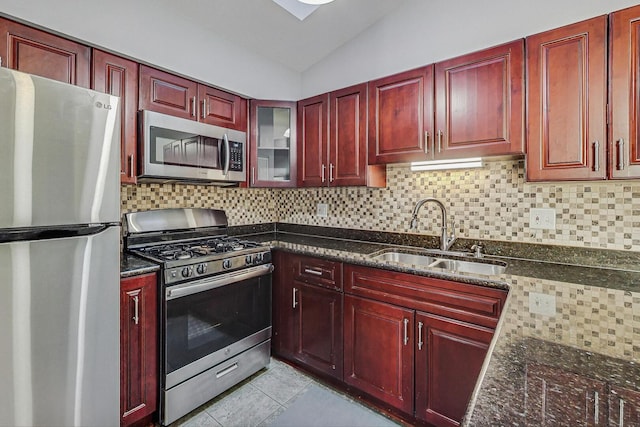 kitchen with a sink, vaulted ceiling, appliances with stainless steel finishes, reddish brown cabinets, and backsplash