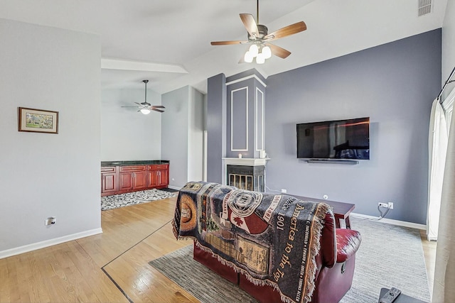 living area featuring visible vents, light wood-style flooring, baseboards, and a glass covered fireplace