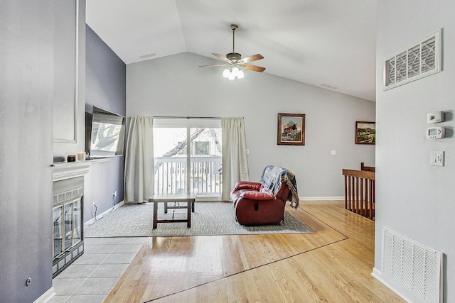 living room featuring a tiled fireplace, vaulted ceiling, light wood-style flooring, and visible vents