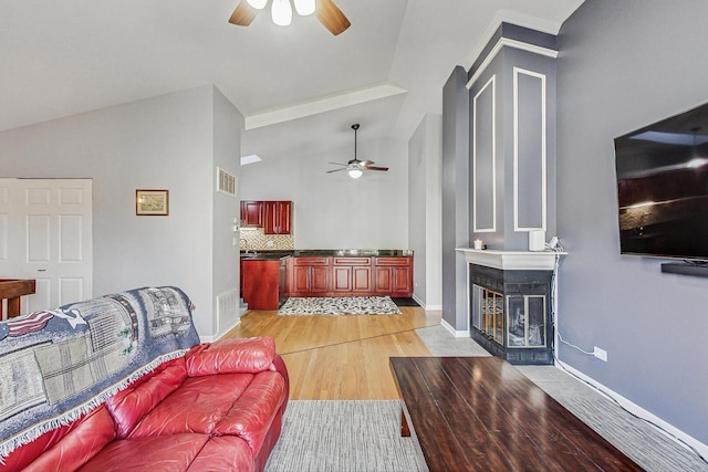 living area featuring baseboards, visible vents, a fireplace with flush hearth, ceiling fan, and light wood-style floors