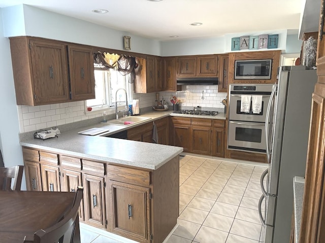 kitchen featuring a sink, under cabinet range hood, appliances with stainless steel finishes, a peninsula, and light countertops