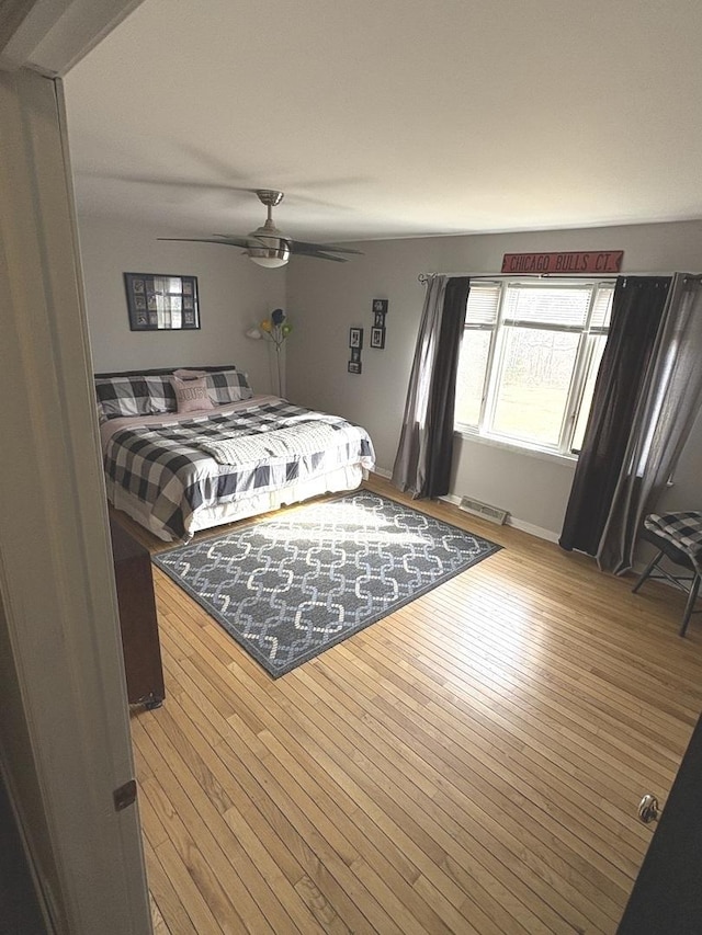 bedroom featuring visible vents, baseboards, a ceiling fan, and wood-type flooring