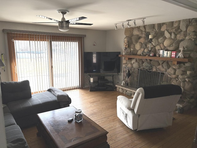 living room featuring a stone fireplace, track lighting, ceiling fan, and hardwood / wood-style floors