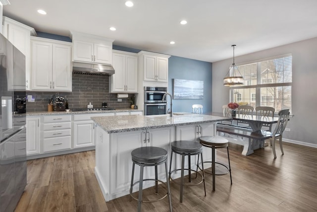 kitchen with under cabinet range hood, white cabinets, tasteful backsplash, and light wood-style flooring