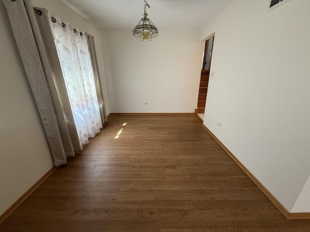 unfurnished dining area featuring wood finished floors, baseboards, and a chandelier