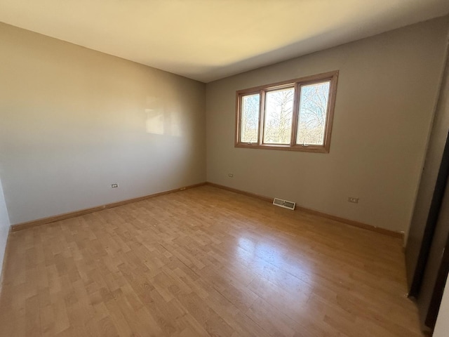 spare room featuring light wood finished floors, visible vents, and baseboards