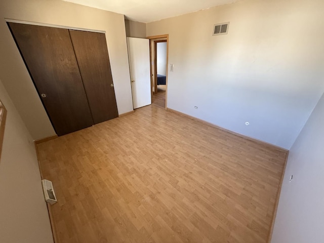 unfurnished bedroom with visible vents, baseboards, a closet, and light wood finished floors