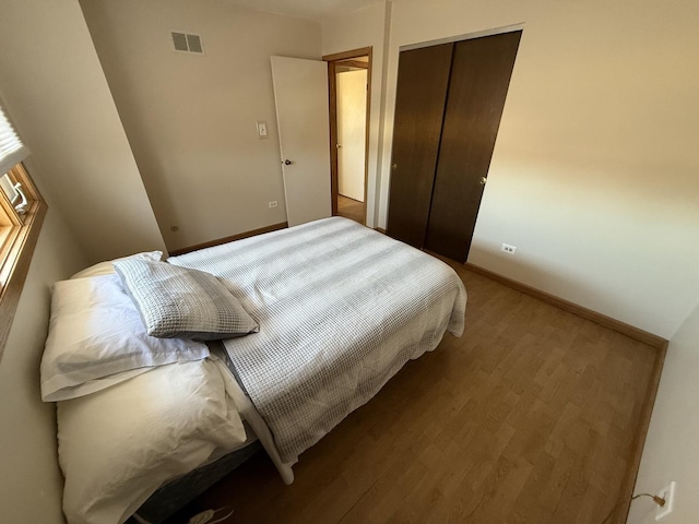 bedroom featuring a closet, visible vents, baseboards, and wood finished floors