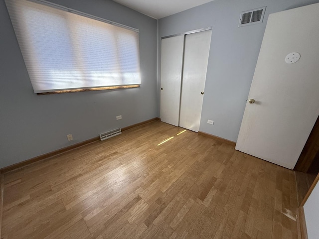 unfurnished bedroom featuring light wood-style floors, visible vents, a closet, and baseboards