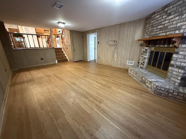 unfurnished living room featuring visible vents, baseboards, stairway, a fireplace, and wood finished floors