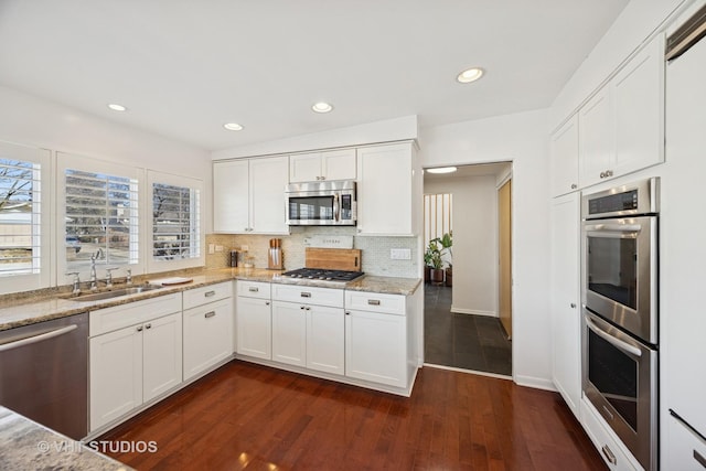 kitchen featuring a sink, light stone counters, backsplash, appliances with stainless steel finishes, and white cabinets