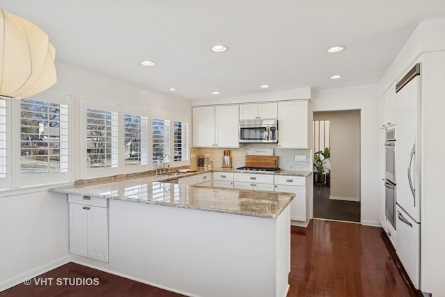 kitchen with light stone countertops, a peninsula, decorative backsplash, white cabinetry, and stainless steel microwave