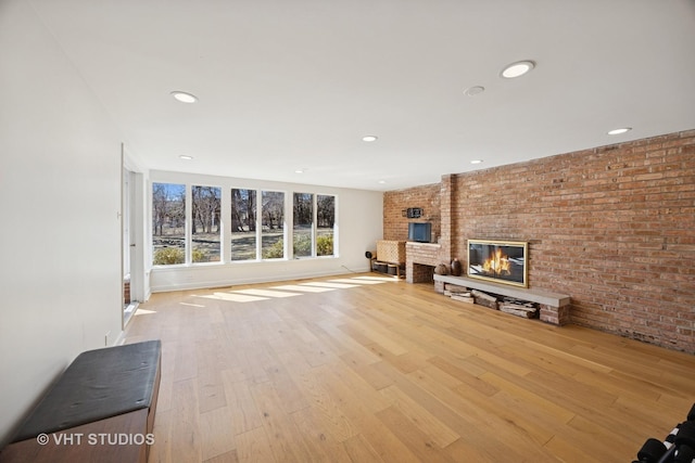 unfurnished living room featuring wood finished floors, baseboards, brick wall, recessed lighting, and a brick fireplace