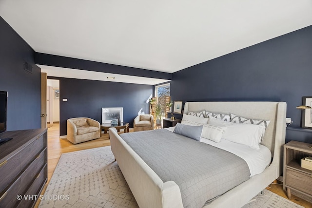 bedroom featuring light wood-type flooring, visible vents, and an accent wall