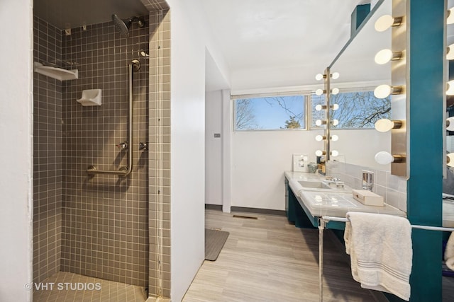 bathroom with tiled shower, vanity, baseboards, and wood finished floors