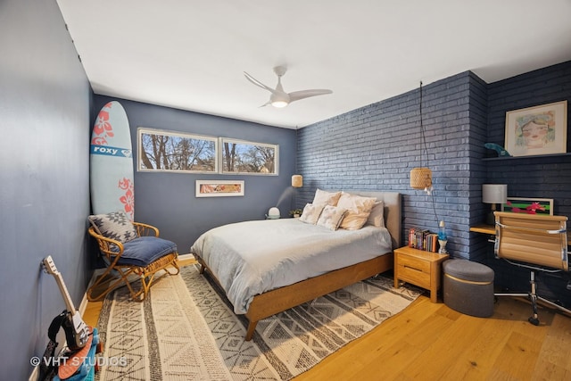 bedroom featuring baseboards, brick wall, wood finished floors, and a ceiling fan