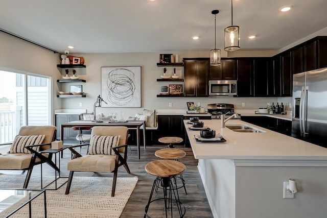 kitchen featuring a kitchen island with sink, stainless steel appliances, a sink, light countertops, and open shelves