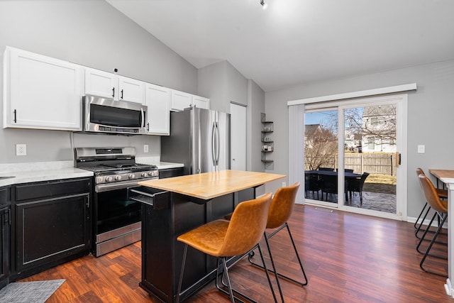 kitchen with a kitchen bar, dark wood-style floors, stainless steel appliances, white cabinets, and vaulted ceiling