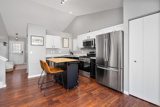 kitchen with butcher block countertops, a sink, a kitchen breakfast bar, a kitchen island, and appliances with stainless steel finishes