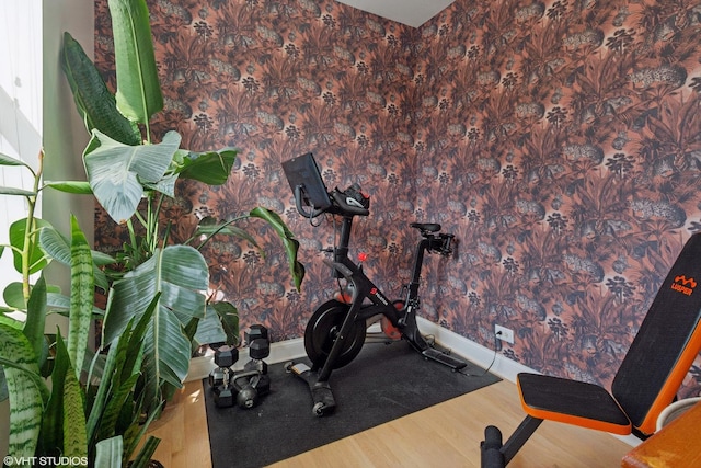 exercise area with wallpapered walls, wood finished floors, and baseboards