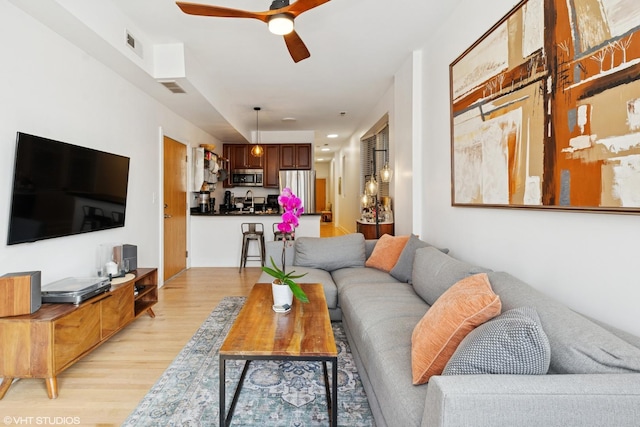 living room featuring light wood-style flooring, a ceiling fan, and visible vents