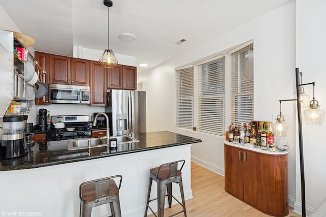 kitchen with light wood finished floors, a peninsula, hanging light fixtures, stainless steel appliances, and a sink