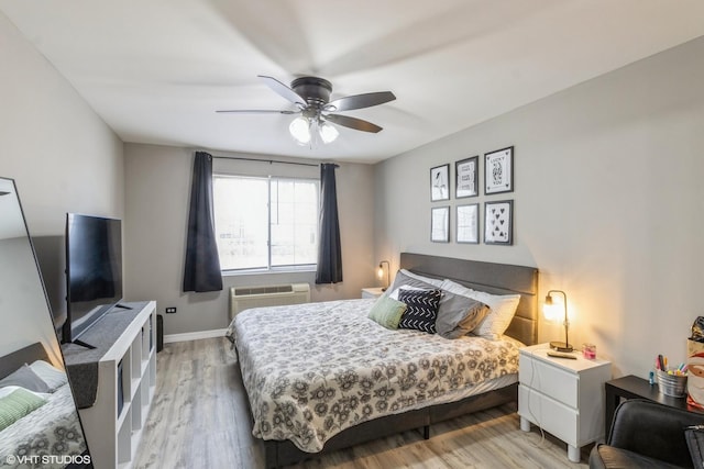 bedroom featuring light wood-style flooring, a ceiling fan, baseboards, and a wall mounted air conditioner