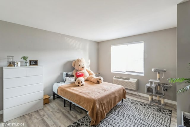 bedroom featuring light wood-style flooring, baseboards, and a wall unit AC