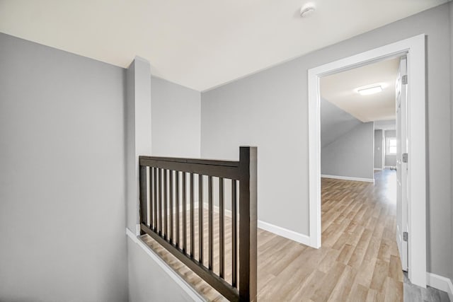 corridor with lofted ceiling, an upstairs landing, light wood-style floors, and baseboards