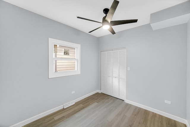 unfurnished bedroom featuring wood finished floors, baseboards, visible vents, ceiling fan, and a closet