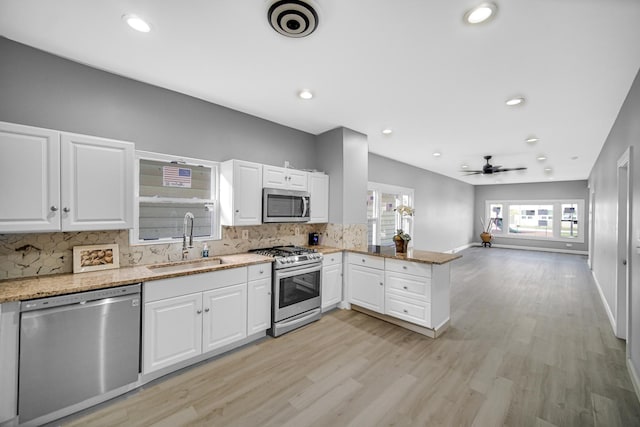 kitchen with light stone counters, a peninsula, a sink, stainless steel appliances, and tasteful backsplash