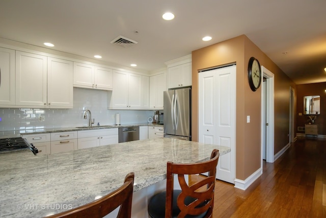 kitchen featuring visible vents, a peninsula, a sink, stainless steel appliances, and white cabinetry