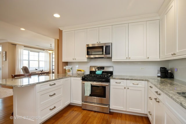 kitchen with wood finished floors, a peninsula, recessed lighting, appliances with stainless steel finishes, and white cabinetry