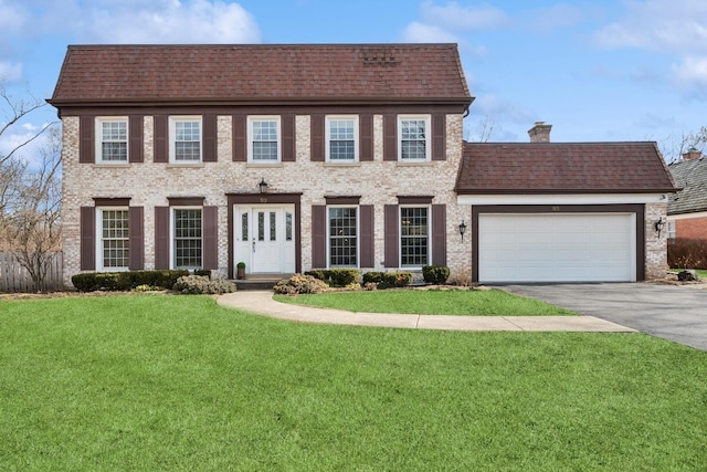 colonial house with brick siding, driveway, a front lawn, and a garage