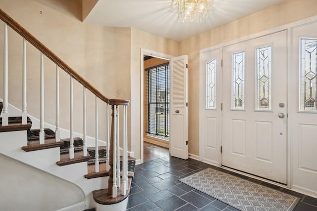 foyer entrance featuring stairs, stone tile floors, a notable chandelier, and baseboards